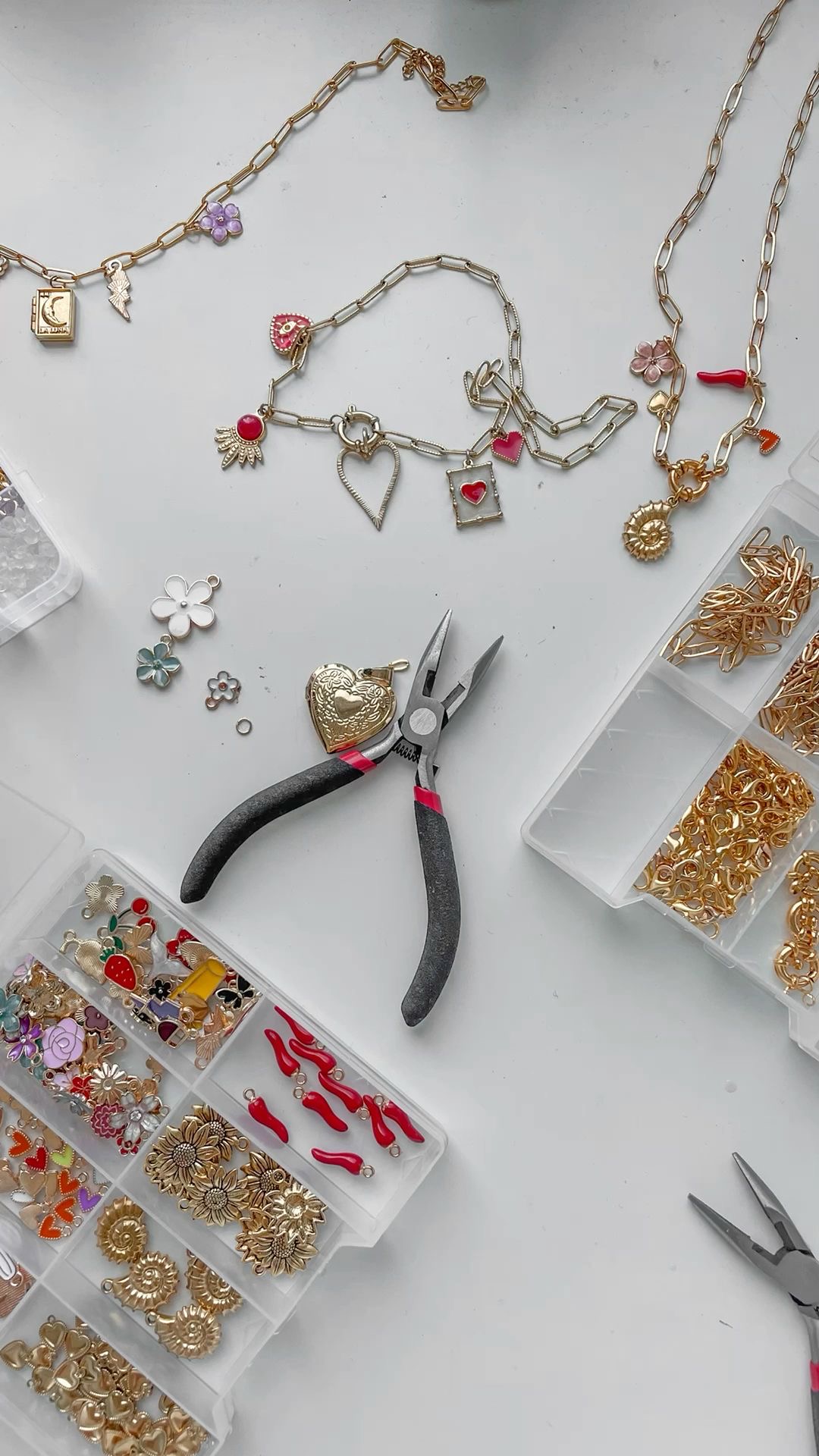 Gold charm necklaces in progress with heart, sun and flower charms