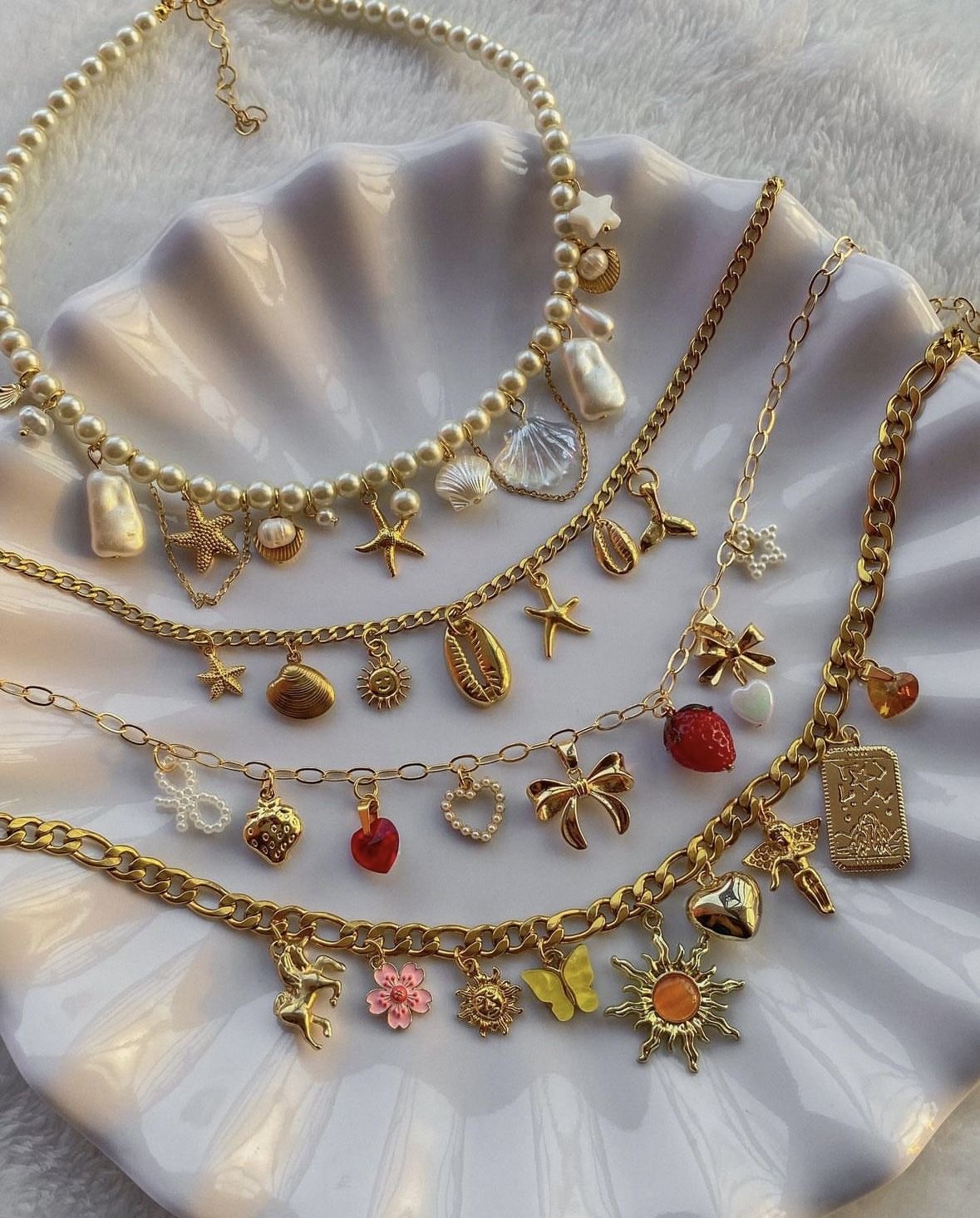 Layered gold pearl and charm necklaces in a shell dish